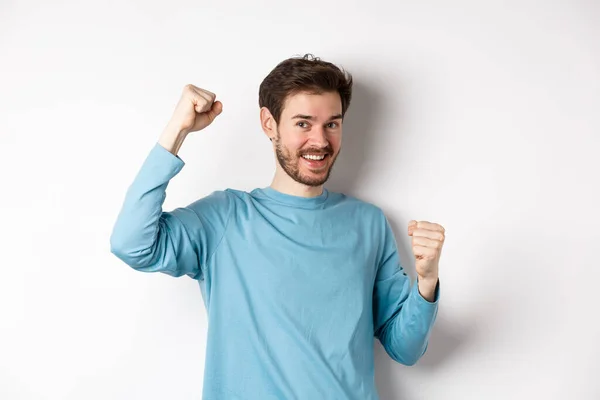 Homem barbudo feliz celebrando a vitória, levantando as mãos para cima e triunfando, ganhando prêmio e sorrindo com alegria, de pé sobre fundo branco — Fotografia de Stock