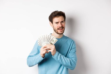 Yakışıklı genç adam para gösteriyor ve memnun görünüyor. Dolarla dans eden, para kazanan, beyaz arka planda duran adam.