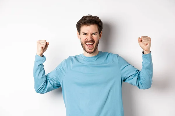 Retrato del hombre guapo satisfecho ganando el premio, regocijándose en el triunfo, celebrando la victoria y gritando sí, de pie sobre fondo blanco — Foto de Stock