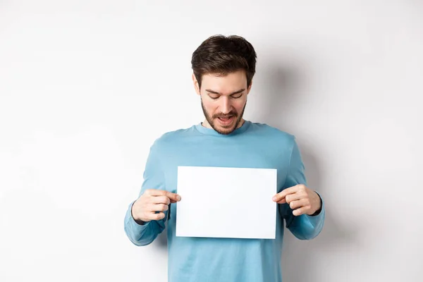 Muchacho barbudo excitado leyendo pancarta en papel en blanco, mostrando el logotipo, de pie sobre fondo blanco — Foto de Stock