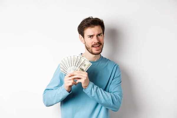 Joven guapo mostrando dinero y luciendo contento. Chico bailando con dólares, ganar ingresos, de pie sobre fondo blanco — Foto de Stock