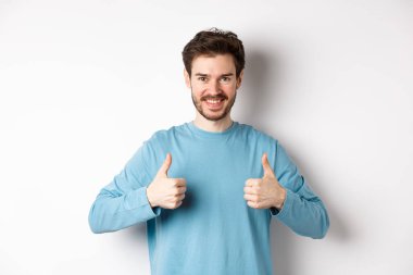 Gülümseyen yakışıklı adam iyi bir seçim yapıyor ve onaylıyor. Övüyor ya da tavsiye ediyor. Beyaz arka planda duruyor.
