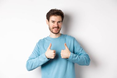 İyi seçim. Çekici beyaz sakallı adam başparmağını kaldırıyor ve gülümsüyor, iyi bir ürünü onaylıyor ve onaylıyor, bir şeyler öneriyor, beyaz arka planda duruyor.