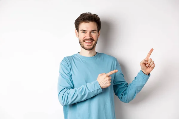 Ευτυχισμένος γενειοφόρος άνδρας δείχνει διαφήμιση, δείχνοντας τα δάχτυλα δεξιά και χαμογελώντας, καλώντας να κάνετε κλικ στο σύνδεσμο, στέκεται πάνω από το λευκό φόντο — Φωτογραφία Αρχείου