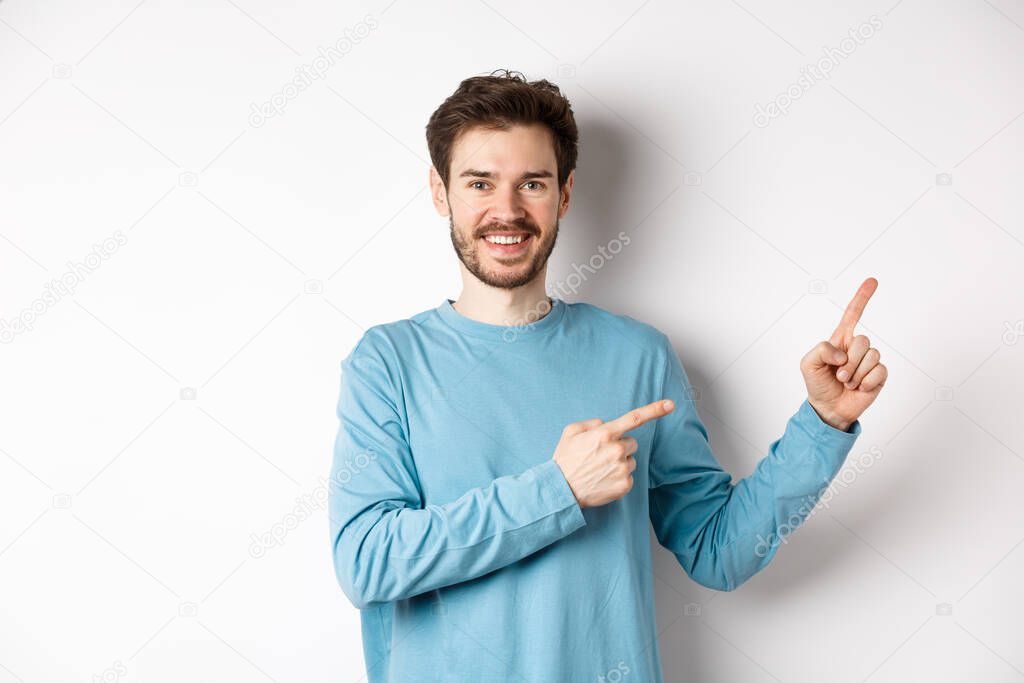 Happy bearded man showing advertisement, pointing fingers right and smiling, inviting to click link, standing over white background