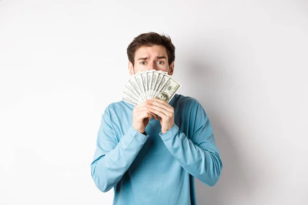 Jovem preocupado olhando com rosto implorando, mostrando dinheiro, de pé em camisola azul sobre fundo branco — Fotografia de Stock
