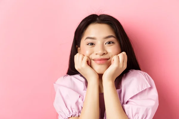 Κοντινό πλάνο του ενθουσιασμένου κοριτσιού από την Ασία που ακούει με ενδιαφέρον, χαμογελά διασκεδάζοντας και κοιτάζοντας την κάμερα, στέκεται πάνω σε ροζ φόντο — Φωτογραφία Αρχείου