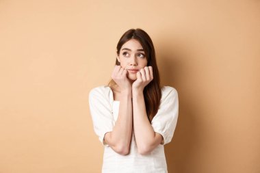 Hayalperest tatlı kadın sol üst köşede dalgın duruyor, romantik bir şeyler düşünüyor, bej arka planda duruyor.