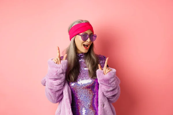 Hipster-Oma in Sonnenbrille und Glitzerkleid posiert für Foto mit Frieden, Siegeszeichen, steht frech vor rosa Hintergrund — Stockfoto