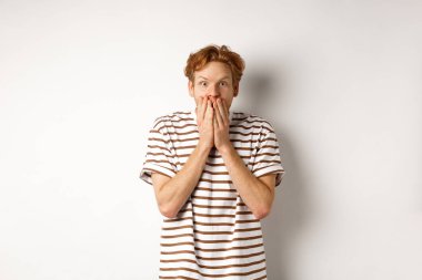 Şaşırmış ve heyecanlı bir adam, kıvırcık saçlı, özel tanıtım teklifini kontrol ediyor, hayranlıkla bakıyor ve hayrete düşüyor, elleriyle ağzını kapatıyor, beyaz arka planda duruyor.