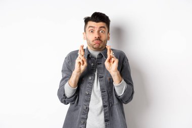 Umut dolu komik adam şans için nefes alıp dua ediyor, dilek tutuyor, haber bekliyor, somurtuyor ve kameraya bakıyor, beyaz arka planda duruyor.