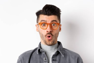 Vay canına, şuraya bak. Heyecanlı, şık gözlüklü yakışıklı adam kameraya bakıyor, beyaz arka planda duran, gözlük mağazası teklifini inceliyor.