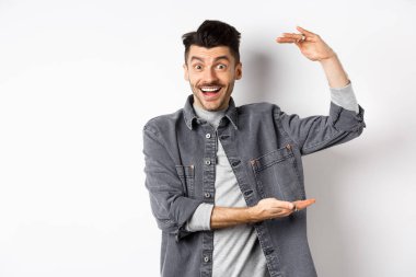 Neşeli adam gülümsüyor ve büyük boy gösteriyor, büyük bir şey gösteriyor ve heyecanlı görünüyor, beyaz arka planda duruyor.