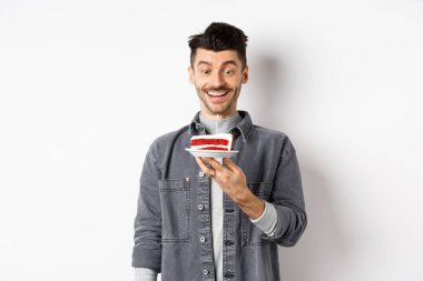 Doğum günü pastasında dilek tutan mutlu çocuk, gülümseyen ve yanan muma bakan heyecanlı, beyaz arka planda duran