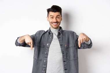 Bıyıklı, mutlu, beyaz bir adam. Gülümsüyor ve özel bir anlaşma yapıyor. Buraya bakmaya davet ediyor, beyaz arka planda duruyor.