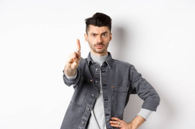 Burada dur. Ciddi bir adam azarlıyor, parmağını sallıyor, kaşlarını çatıyor, kötü bir şeyi onaylamıyor, beyaz arka planda duruyor.