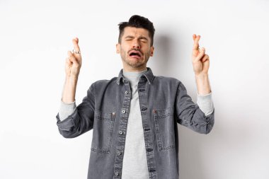 Üzgün ve sefil bir adam, Tanrı 'yı umuyor, dua ediyor, dua ediyor ya da umutsuz bir suratla dilek tutuyor, beyaz arka planda duruyor.