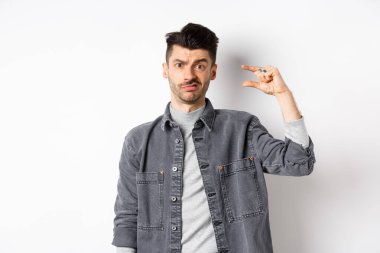 Hayal kırıklığına uğramış, küçük boylarda, suratını buruşturan üzgün, küçük şeylerden rahatsız olan, beyaz arka planda duran biri.