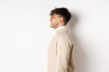 Gözlüklü yakışıklı beyaz adamın profili, boş yere bakıyor neşeli bir gülümsemeyle, beyaz arka planda duruyor.