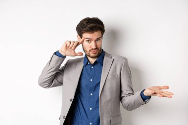 Delirdin mi sen? Takım elbiseli genç adam tuhaf ya da aptalca bir hatayı işaret ederek omuz silkiyor, beyaz arka planda duruyor.