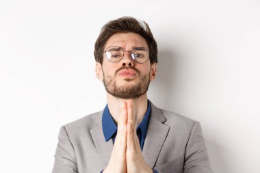 Gözlüklü yapışkan adam son bir iyilik istiyor, yardım dileniyor ve üzgün tatlı bakıyor, beyaz arka planda duruyor.