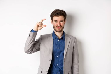 Hayal kırıklığına uğramış işadamı, küçük boyutlarda ve buruşuk suratlı üzgün, az gelirli, beyaz arka planda hoşnutsuz duruyor.