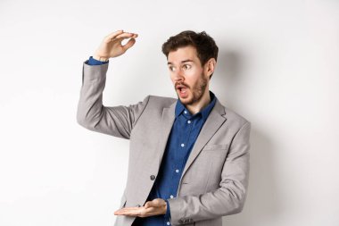 Takım elbiseli yakışıklı bir satıcı, büyük kar elde ediyor, kameraya hevesle gülümsüyor, beyaz arka planda duruyor.