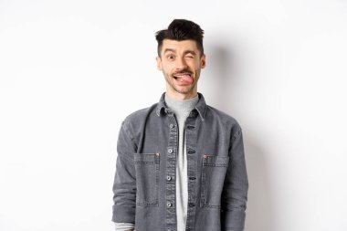 Bıyıklı komik adam dil gösteriyor ve göz kırpıyor, seni güldürüyor, beyaz arka planda duruyor.