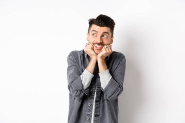 Heyecanlı genç adam sol üst köşede rüya gibi görünüyor, paketi bekliyor, hayal görüyor ya da hayal kuruyor, beyaz arka planda duruyor.