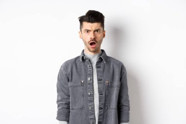 Şok olmuş ve gücenmiş bir adam, kameraya açık ağızla bakıyor, acımasız sözlerle incinmiş, beyaz arka planda hayal kırıklığına uğramış.