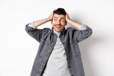 Heyecanlı genç adam rahatlamış ve mutlu görünüyor, gülümsüyor ve logoya bakıyor, el ele tutuşuyor neşeli, beyaz arka planda duruyor.