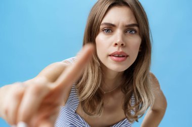 Curious and intrigued woman poking at camera with finger as if checking anyone there looking at her, bending forward with serious interested expression frowning, pressing forefinger to lense clipart