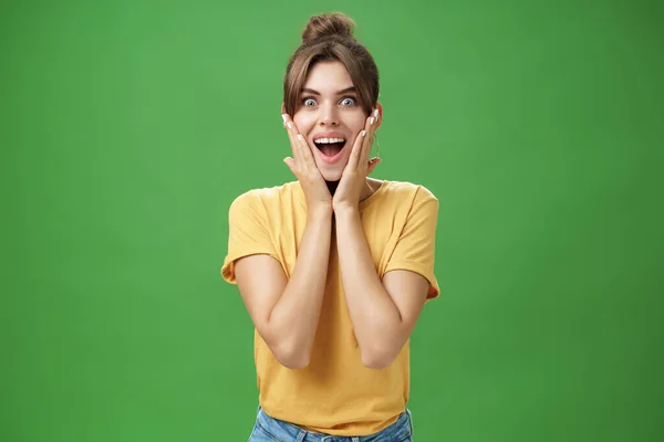Indoor tiro de excitado e surpreendido energizado atraente glamourosa fêmea em amarelo t-shirt tocando bochechas de espanto sorrindo amplamente surpreendido posando sobre fundo verde — Fotografia de Stock
