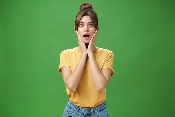 Mujer sintiéndose sorprendida y encantada disfrutando de un buen resultado después de la desintoxicación y la aplicación de mascarilla facial para el cuidado de la piel tocando las mejillas abriendo la boca del asombro y emocionada posando sobre fondo verde —  Fotos de Stock