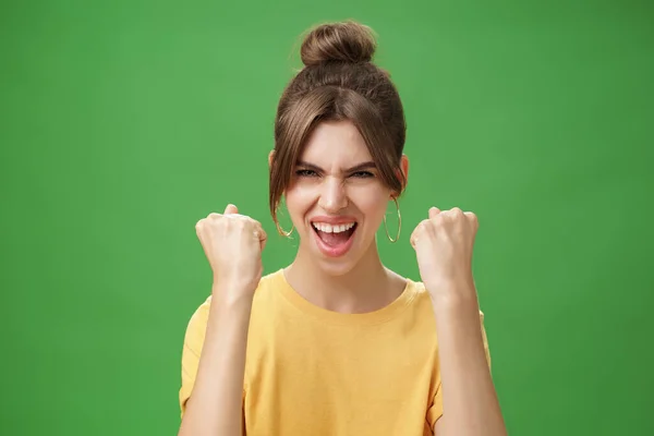 Женщина с духом победителя поднимает сжатые кулаки, улыбаясь взволнованно и поддерживая аплодисменты, готовясь к тренировкам, размахивая конфетами с криком, смело смотрящим на камеру через зеленую стену — стоковое фото