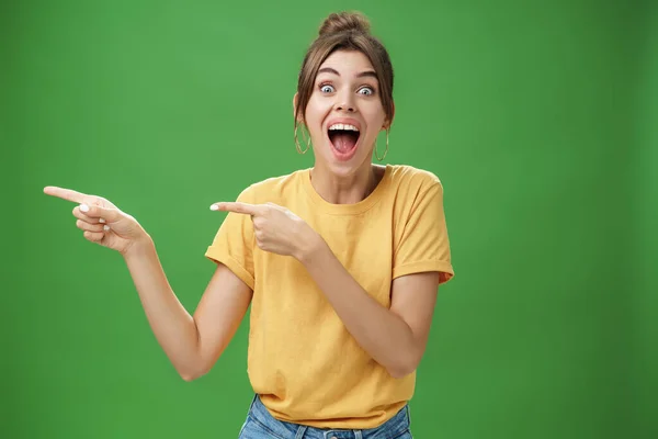 Cintura-up tiro de entusiasmado e carismático impressionado menina feliz rindo e sorrindo amplamente apontando esquerda em engraçado hilariante coisa reagindo surpreso e entretido, posando sobre fundo verde — Fotografia de Stock