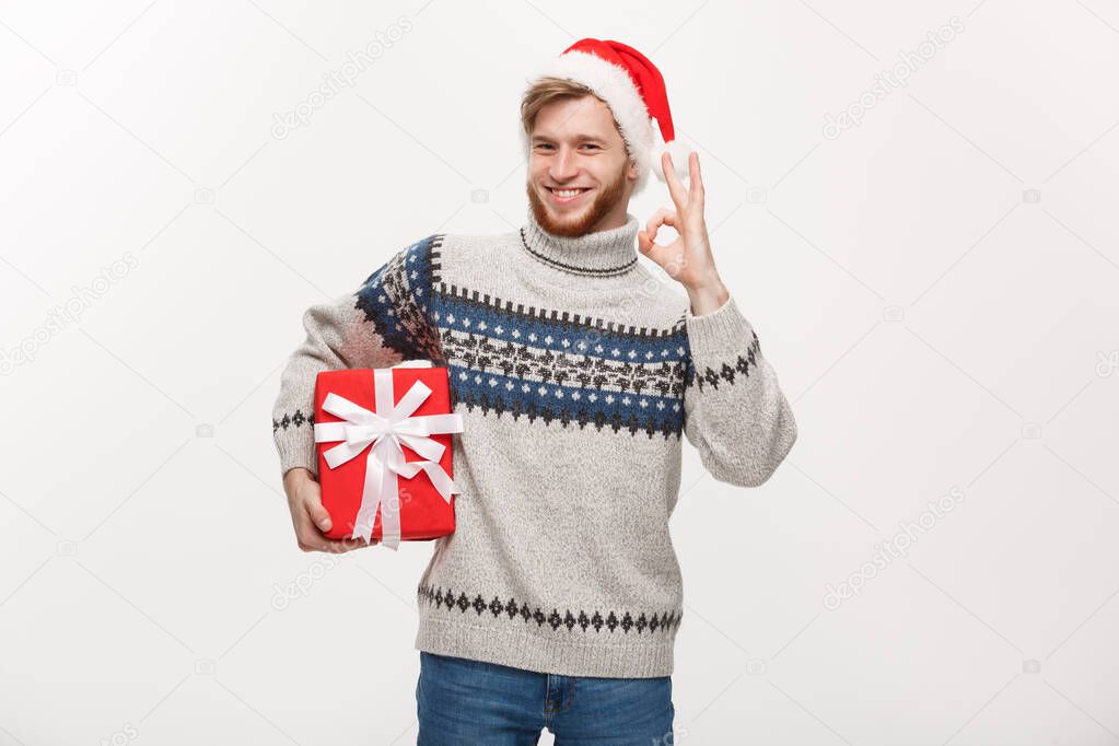 Holiday Concept - Young beard man in sweater holding box and giving ok sign.
