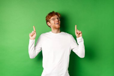 Gözlüklü neşeli yakışıklı adam satış anlaşmasını kontrol ediyor, mutlu ve rüya gibi bir gülümsemeyle yukarı bakıyor, yeşil arka planda duruyor.