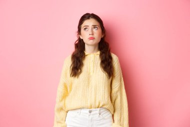 Üzgün ve kasvetli genç bir kadının üzgün bir yüz ifadesi. Pişmanlıkla ya da kıskançlıkla yukarı bakıyor. Pembe arka planda hayal kırıklığına uğramış duruyor.