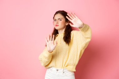 Lütfen dur, yeter. Memnuniyetsiz ve gönülsüz genç kadın geride dur, blok hareketi yap, ellerini uzat ve reddet ve hayır de, pembe arka planda dur.