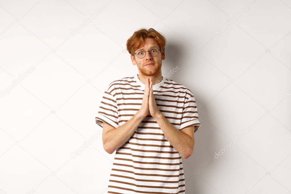 Cute redhead man in glasses asking for help, pleading and looking clingy at camera, begging for favour, white background