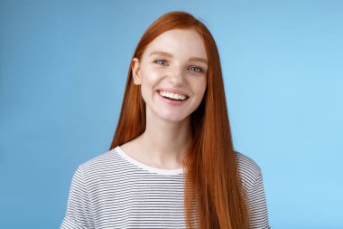 Mutlu dost canlısı, neşeli, neşeli, 20 'li yaşlardaki, samimi, kızıl saçlı, neşeli, gülen, şakacı, sırıtan, neşeli, şanslı tavır sergileyen, mavi arka planda duran kız.