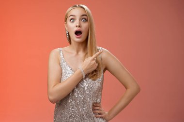 Nutku tutulmuş Avrupalı blong kız, çenesini indir sağ üst köşeyi işaret eden heyecanlı gözler, şaşkın kırmızı arka plan, dedikoducu zengin barmen, parlak elbiseler giyiyor.