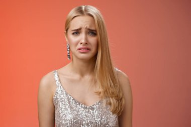 Hayal kırıklığına uğramış, gümüş renkli şık elbiseli, suratını buruşturan tatlı sarışın kadın üzgün, üzgün üzgün üzgün üzgün, mutsuz, kalbi kırık, kötü, kırmızı arka plan