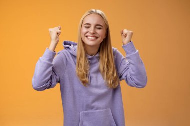 Pozitif saçlı genç kadın kazananın zaferini kutlarken ellerini kaldır zafer elde etmek için ellerini yumruk at. Gözlerini kapat ve gülümseyerek büyük teklifi kabul et, başarıya ulaş.