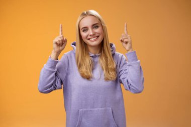 Yardımsever, arkadaş canlısı, destekleyici, çekici, yeni ürün reklamı gösteren çekici bir bayan arkadaş başını eğen, gülümseyen, turuncu arka plan.