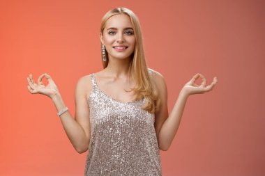 Rahatlamış, mutlu, zarif, gümüş renkli, şık elbiseli, mutlu, genç bir kadın. Rahat kırmızı zemin üzerinde duruyor. Nirvanaya uzan ve huzurlu, meditasyon yaparken gülümse.