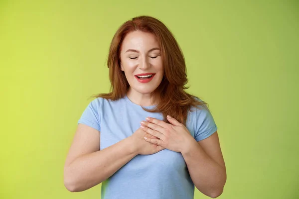 Gefascineerde schattige roodharige gepassioneerde vrouw van middelbare leeftijd zucht mooie aanraking hart sluit ogen glimlachen blij expressie bewondering verleiding gevoel waardering dankbare emoties groene achtergrond — Stockfoto