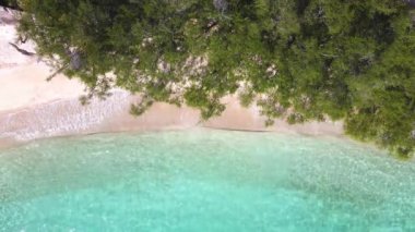 Okyanus mavi dalgalarının havadan görünüşü kumsalda kırılıyor. Deniz dalgaları ve güzel kumsal manzaralı insansız hava aracı görüntüleri. Kuş bakışı okyanus dalgaları yukarıdan boş bir kumsala çarpıyor.
