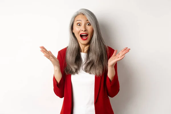 Affärsmän. Överraskad senior asiatisk kvinnlig entreprenör, kippar förvånad, stirrar på kameran, höra goda nyheter, står glad över vit bakgrund — Stockfoto